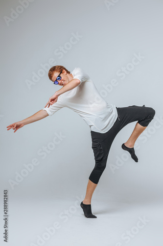 Red-haired man in sunglasses and a white t-shirt dancing on a light background