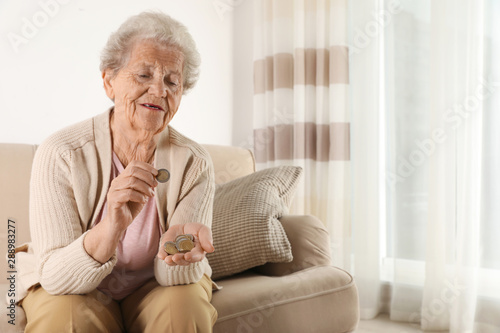 Elderly woman counting coins in living room. Space for text
