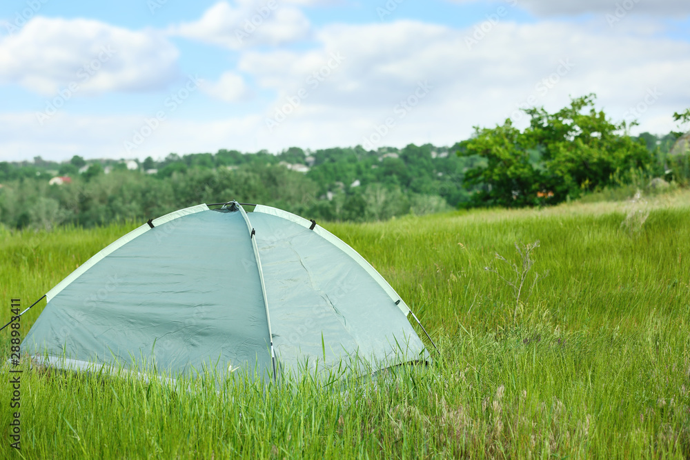 Modern camping tent in green field on sunny day. Space for text