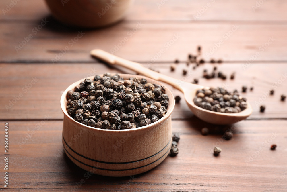Bowl of black pepper corns and spoon on wooden table, space for text Bowl of black pepper corns and spoon on wooden table, space for text