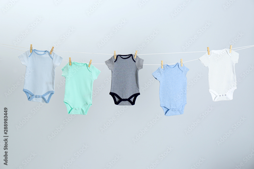 Different baby onesies hanging on clothes line against light grey background. Laundry day Different baby onesies hanging on clothes line against light grey background. Laundry day