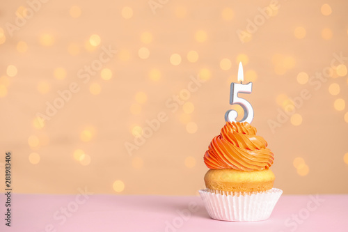Birthday cupcake with number five candle on table against festive lights, space for text