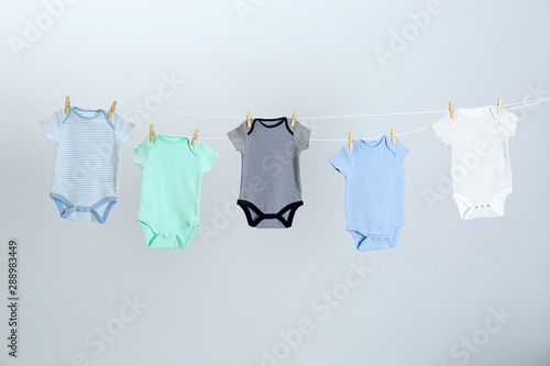 Different baby onesies hanging on clothes line against light grey background. Laundry day