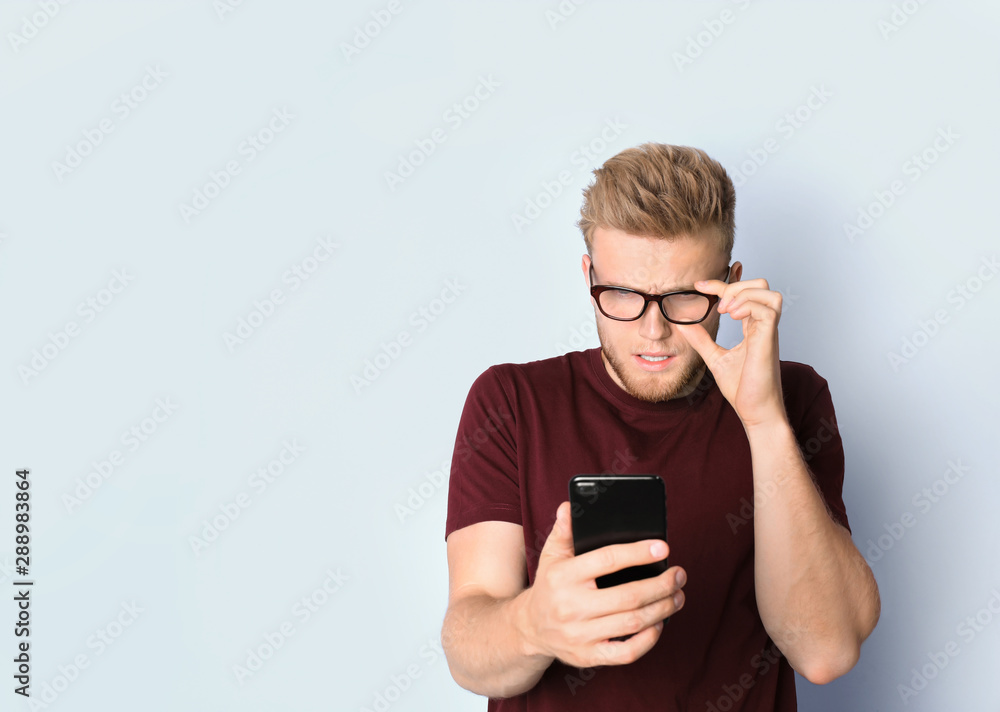 Young man with glasses using mobile phone on light background. Vision problem Young man with glasses using mobile phone on light background. Vision problem