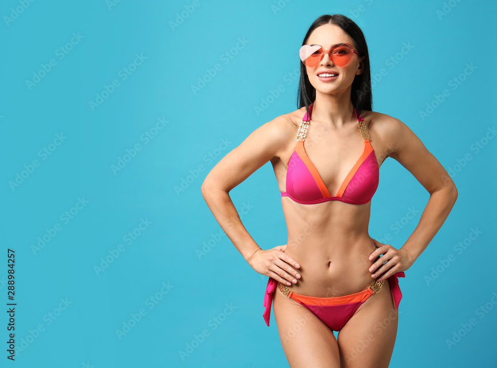 Obraz premium Beautiful young woman in stylish bikini with sunglasses on light blue background. Space for text