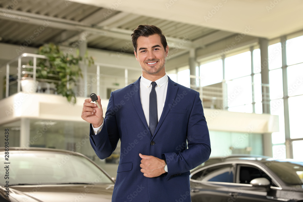 Young salesman with car key in modern dealership