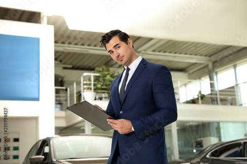 Young salesman with clipboard near car in modern dealership © New Africa