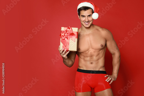 Canvas Print Sexy shirtless Santa Claus with gift on red background, space for text