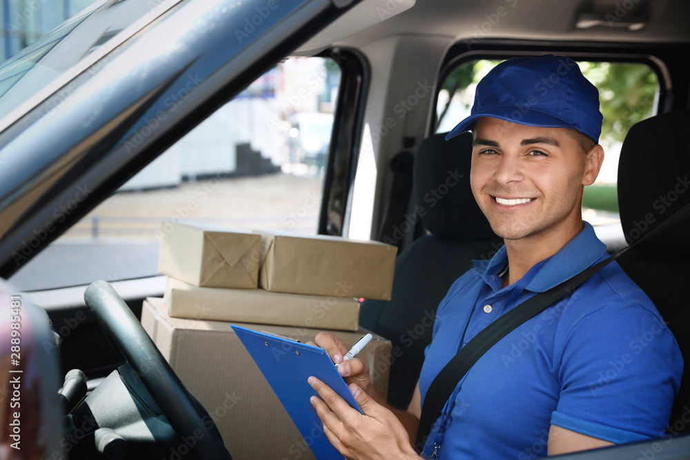Young courier with parcels and clipboard in delivery car Young courier with parcels and clipboard in delivery car