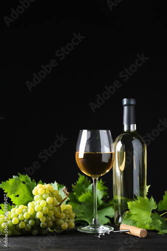 Fresh ripe juicy grapes with wineglass on grey table against black background, space for text