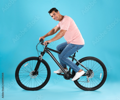 Handsome young man with modern bicycle on light blue background