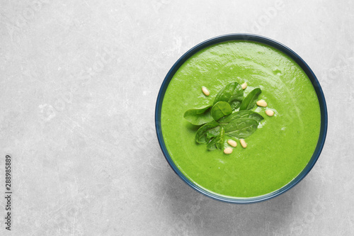 Bowl of healthy green soup with fresh spinach on grey table, top view. Space for text