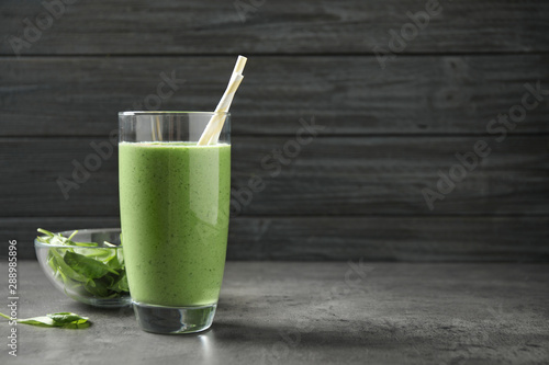 Glass of healthy green smoothie with fresh spinach on grey table. Space for text