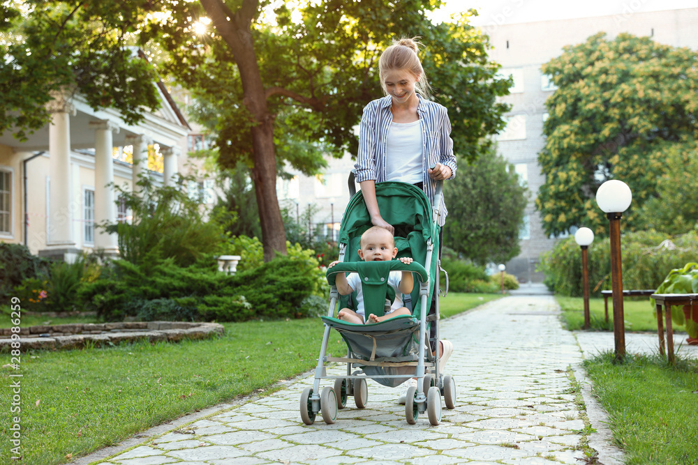 Teen nanny with cute baby in stroller walking in park. Space for text Teen nanny with cute baby in stroller walking in park. Space for text