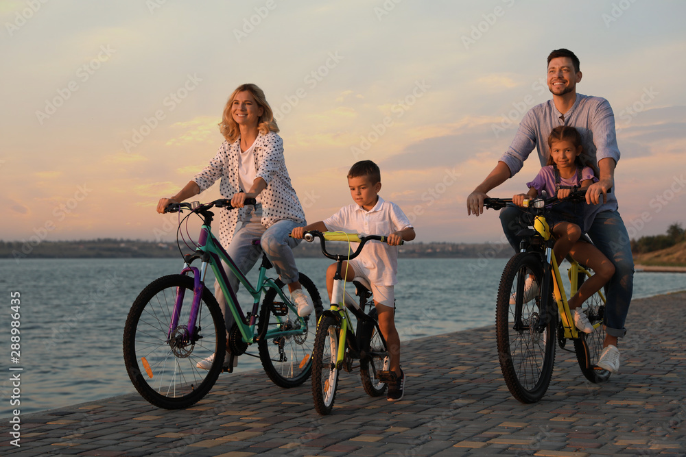 Happy family with children riding bicycles near river at sunset