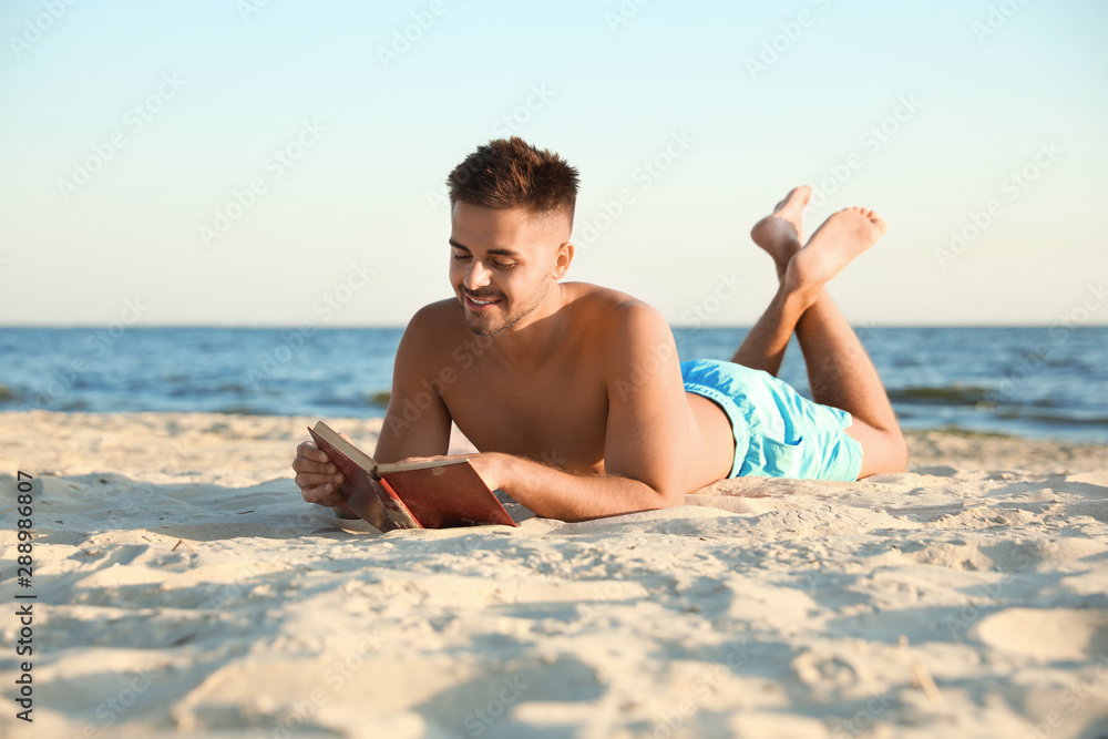 Young man reading book on sandy beach near sea Young man reading book on sandy beach near sea