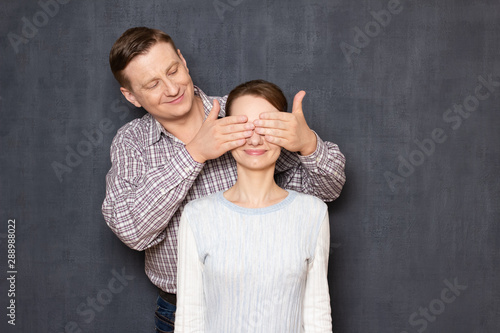 Studio shot of happy man covering eyes of cheerful woman