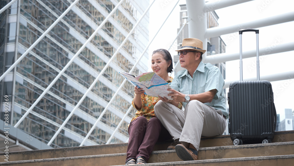 Asian Senior couple are sitting holding the map to search for destinations the streets of the big city. Elderly retired tourists spend the holidays to travel abroad. Travelers and lifestyle concept.