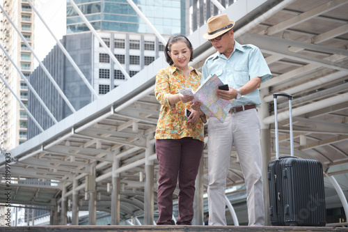 Asian Senior couple are standing holding the map to search for destinations the streets of the big city. Elderly tourists spend the holidays to travel abroad. Travelers and lifestyle concept. © JuYochi