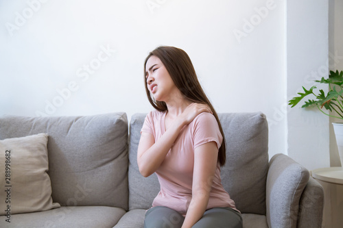 Young woman with shoulder pain. Young woman suffering shoulder neck ache tired sit on sofa at home.