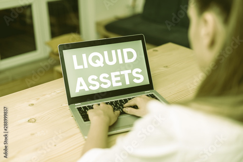 Conceptual hand writing showing Liquid Assets. Concept meaning Cash and Bank Balances Market Liquidity Deferred Stock woman with laptop smartphone and office supplies technology