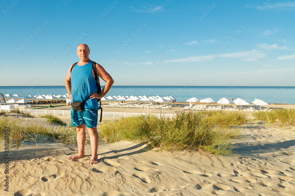 A man in shorts and a T-shirt on the beach against the background of the sea.