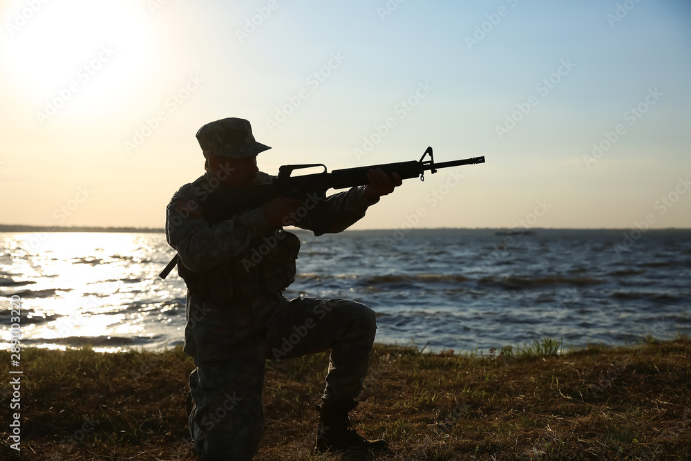Silhouette of soldier in camouflage taking aim near river Silhouette of soldier in camouflage taking aim near river