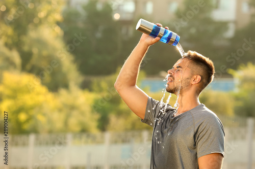 Handsome sporty man refreshing himself with water after training outdoors photo