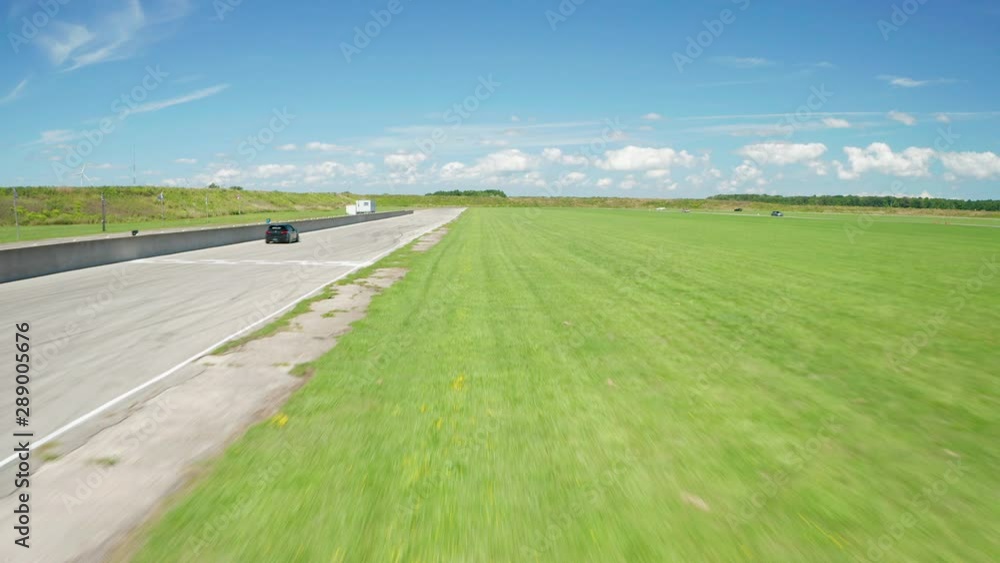 Drone following a car down an open straightaway on a race track Drone following a car down an open straightaway on a race track