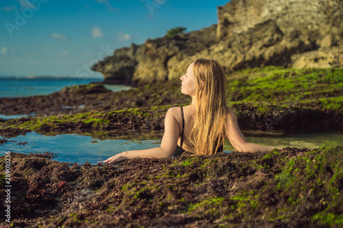 Young woman tourist on Pantai Tegal Wangi Beach sitting in a bath of sea water, Bali Island, Indonesia. Bali Travel Concept