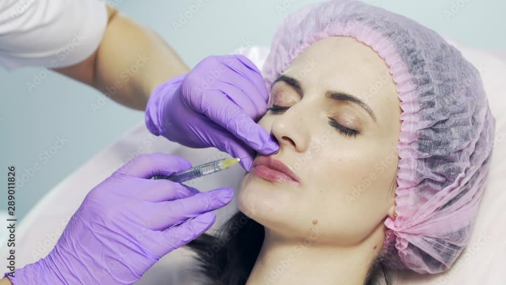 Beautiful woman is getting an injection in her lips in clinic. Cosmetologist in gloves pricks female's lips with syringe Beautiful woman is getting an injection in her lips in clinic. Cosmetologist in gloves pricks female's lips with syringe