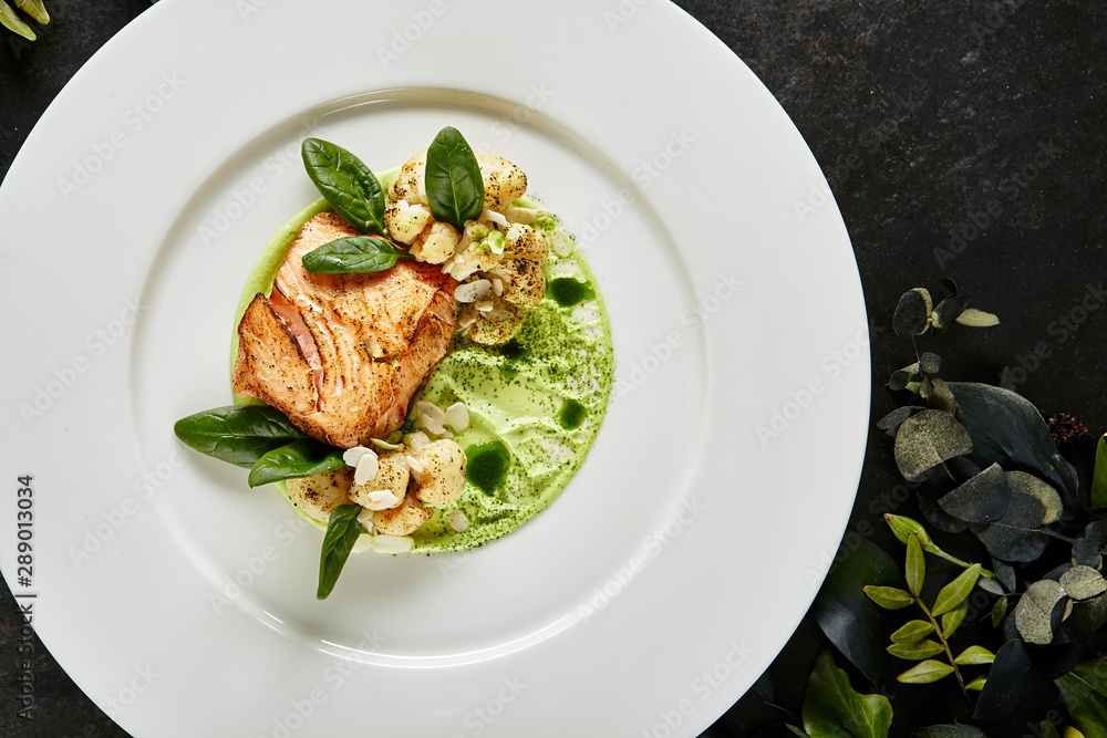 Exquisite Serving White Restaurant Plate with Fillet of Salmon 48 Degrees, Green Peas Cream and Burnt Cauliflower Top View. Stylish Italian Seafood Dish on Natural Black Marble Background Exquisite Serving White Restaurant Plate with Fillet of Salmon 48 Degrees, Green Peas Cream and Burnt Cauliflower Top View. Stylish Italian Seafood Dish on Natural Black Marble Background