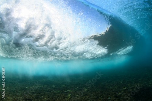 dramatic crashing wave underwater on a shallow reef with sunrays through the water