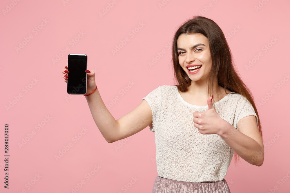 Laughing young woman in casual light clothes posing isolated on pink background in studio. People lifestyle concept. Mock up copy space. Holding mobile phone with blank empty screen, showing thumb up. Laughing young woman in casual light clothes posing isolated on pink background in studio. People lifestyle concept. Mock up copy space. Holding mobile phone with blank empty screen, showing thumb up.