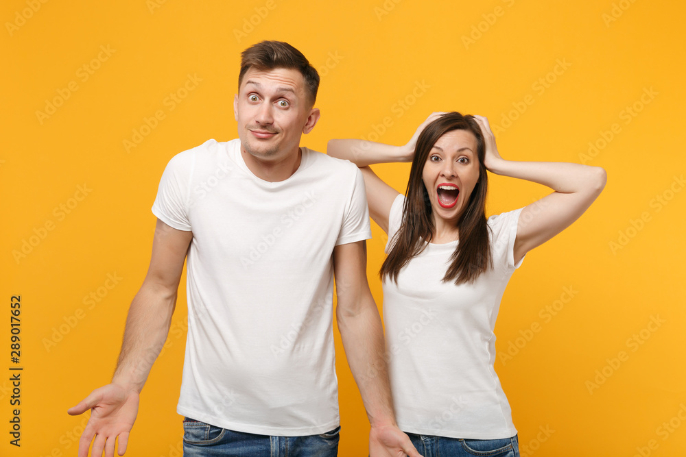 Young couple two friends guy girl in white empty blank design t-shirts posing isolated on yellow orange background. People lifestyle concept. Mock up copy space. Putting hands on head, spreading arms. Young couple two friends guy girl in white empty blank design t-shirts posing isolated on yellow orange background. People lifestyle concept. Mock up copy space. Putting hands on head, spreading arms.