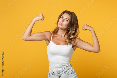 Strong young woman girl in light casual clothes posing isolated on yellow orange wall background studio portrait. People sincere emotions lifestyle concept. Mock up copy space. Showing biceps muscles.