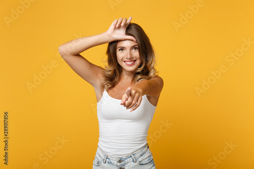 Cheerful young woman girl in light casual clothes posing isolated on yellow orange wall background. People lifestyle concept. Mock up copy space. Showing loser gesture pointing index finger on camera.