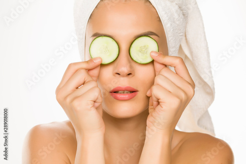 Young woman posing with slices of cucumbers on her eyes on white background
