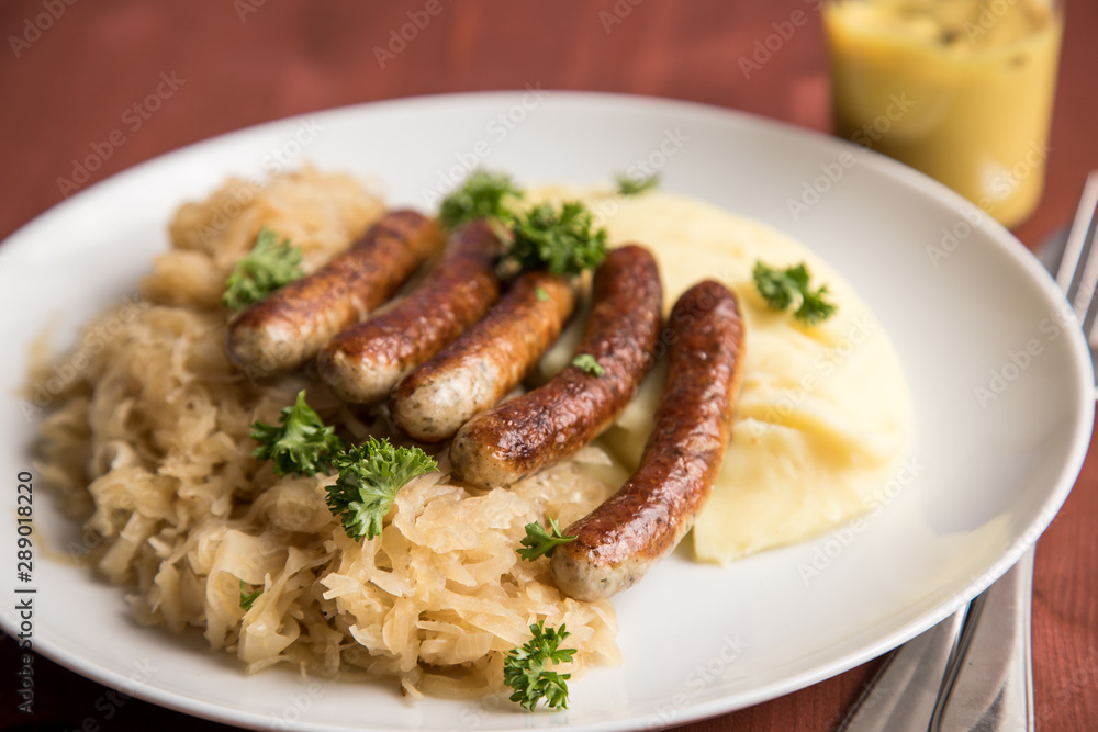 Kleine Bayrische Nürnberger Rostbratwürste mit Sauerkraut, Kartoffelpüree und Senf auf Holz Tisch Hintergrund Kleine Bayrische Nürnberger Rostbratwürste mit Sauerkraut, Kartoffelpüree und Senf auf Holz Tisch Hintergrund