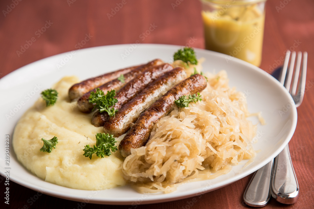 Kleine Bayrische Nürnberger Rostbratwürste mit Sauerkraut, Kartoffelpüree und Senf auf Holz Tisch Hintergrund Kleine Bayrische Nürnberger Rostbratwürste mit Sauerkraut, Kartoffelpüree und Senf auf Holz Tisch Hintergrund