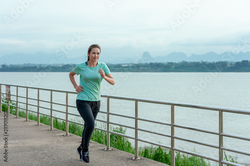 Young fitness Asian woman is running and jogging an outdoor workout on the riverwalk in the morning for lifestyle health. © ParinPIX