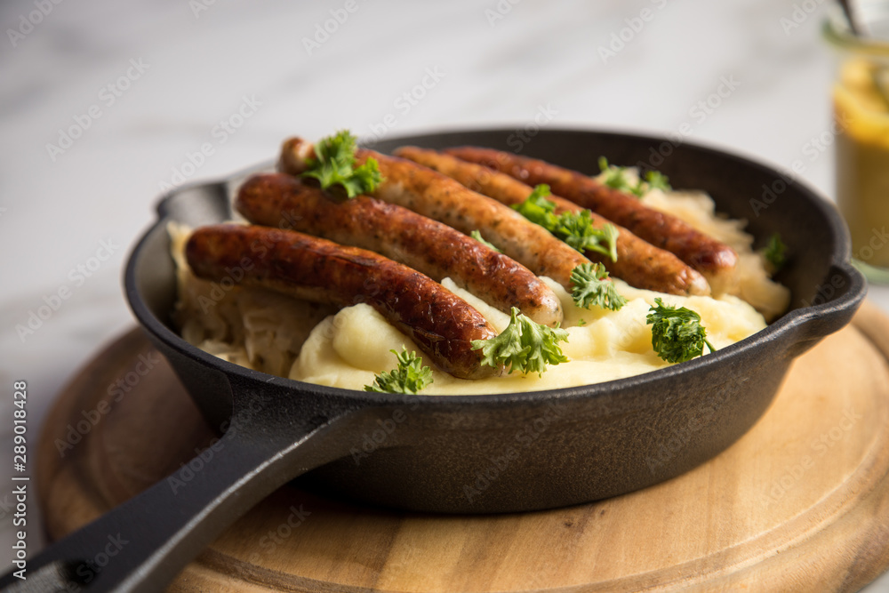 Kleine Bayrische Nürnberger Rostbratwürste mit Sauerkraut, Kartoffelpüree und Senf in rustikaler Gusseisenpfanne auf Holz Brett und Marmor Tisch Kleine Bayrische Nürnberger Rostbratwürste mit Sauerkraut, Kartoffelpüree und Senf in rustikaler Gusseisenpfanne auf Holz Brett und Marmor Tisch
