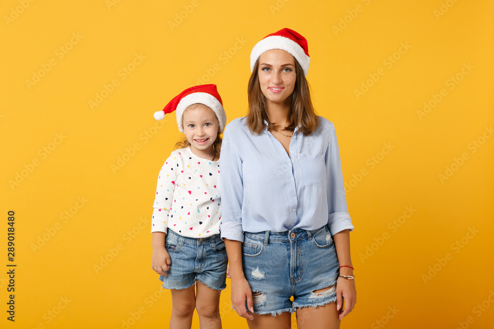Fototapeta premium Woman child baby girl 4-5 years old in Christmas Santa hat. Mommy little kid daughter isolated on yellow background studio portrait. Happy New Year 2020 celebration holiday concept. Mock up copy space