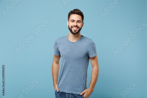 Young smiling handsome man in casual clothes posing isolated on blue wall background, studio portrait. People sincere emotions lifestyle concept. Mock up copy space. Holding hands in pockets.