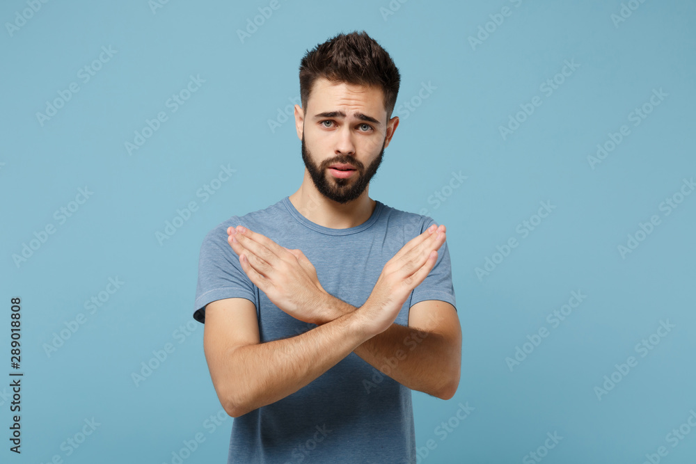 Young puzzled man in casual clothes posing isolated on blue wall background, studio portrait. People sincere emotions lifestyle concept. Mock up copy space. Showing stop gesture with crossed hands. Young puzzled man in casual clothes posing isolated on blue wall background, studio portrait. People sincere emotions lifestyle concept. Mock up copy space. Showing stop gesture with crossed hands.