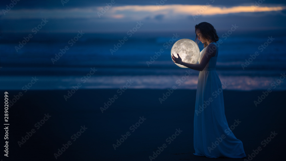 Tender image of a girl. Female magic. Beautiful attractive girl in full growth on a night beach with sand hugs the moon, art photo. On a dark background with space. Riddle, astrology, zodiac. Banner. - obrazy, fototapety, plakaty 