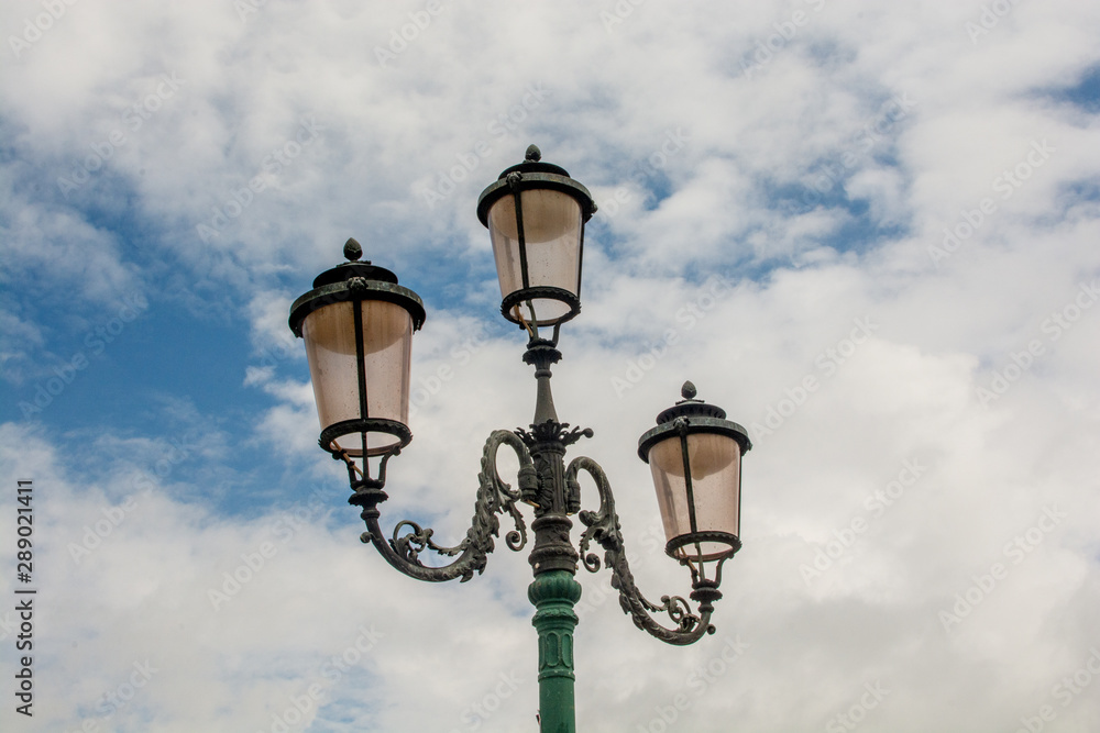 Venice old-fashioned retro lamps made of copper and pink glass with cloudy blue sky on the background Venice old-fashioned retro lamps made of copper and pink glass with cloudy blue sky on the background