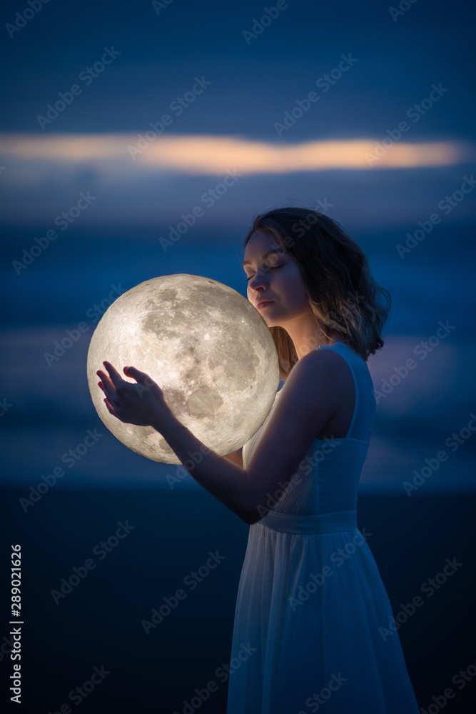 Naklejka premium delikatny obraz anioła, dziewczyny z księżycem w rękach na nocnej plaży. fotografia artystyczna. Bajka i zagadka. Astrologia i znaki zodiaku.