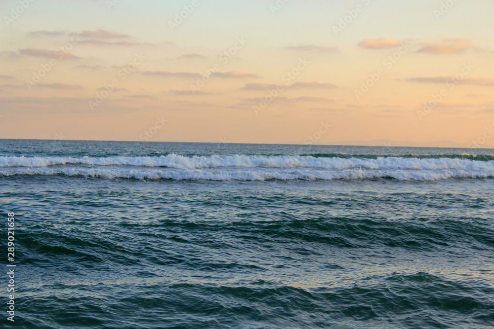 White waves running on a blue sea against a pink sunset sky White waves running on a blue sea against a pink sunset sky