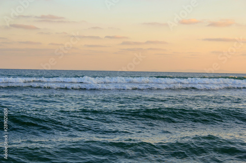 White waves running on a blue sea against a pink sunset sky